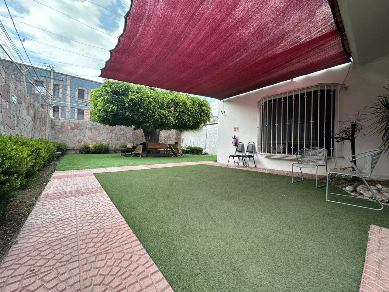 Jardín con áreas verdes, bancas y árboles donde los residentes conviven y toman el sol